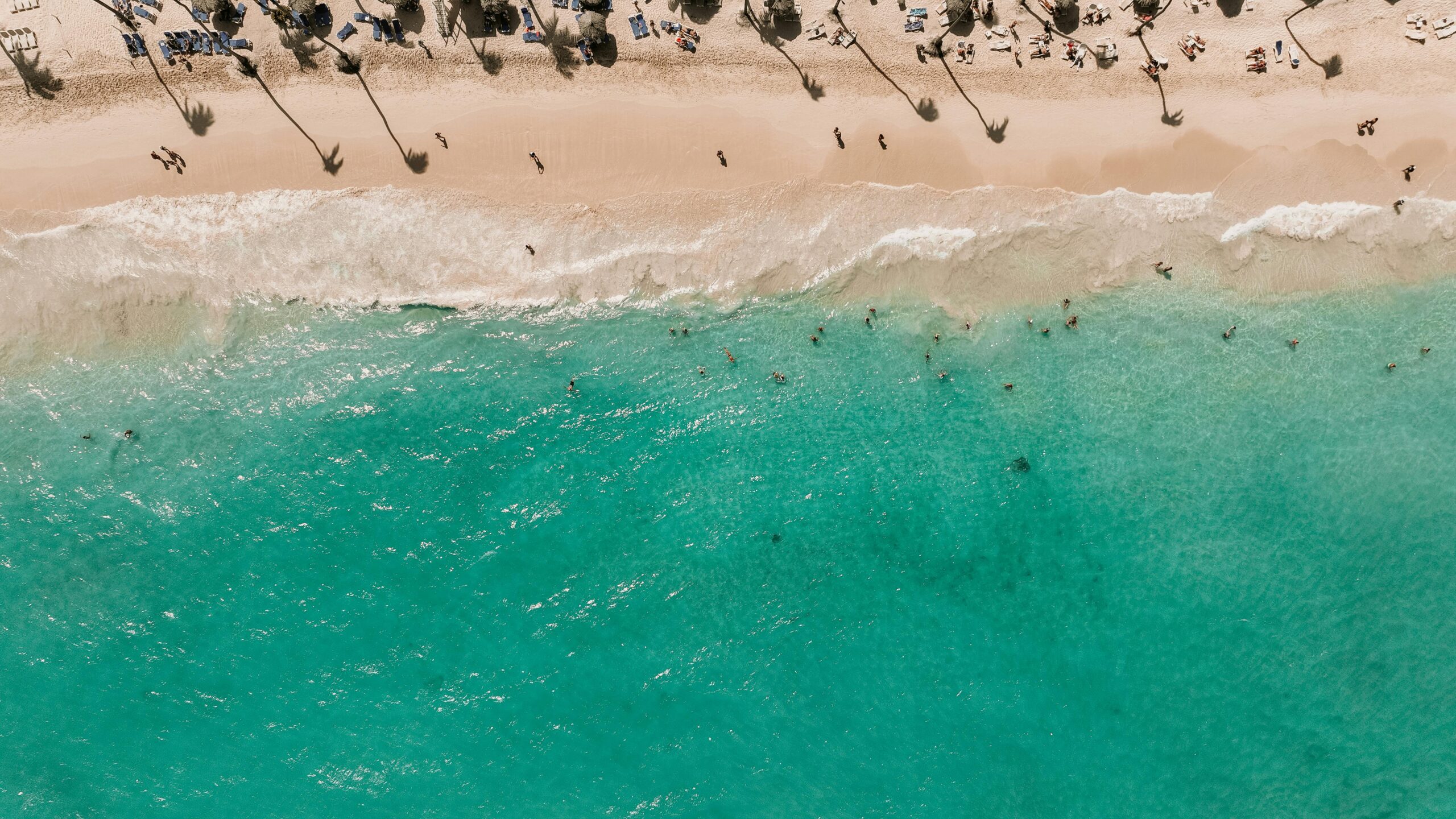 Drone view of a lively beach with turquoise waters and sunbathing tourists, perfect for a summer getaway.